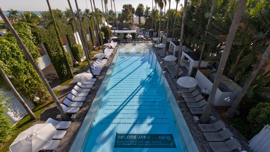 Aerial view of the Delano Hotel pool with a page of Decoded printed across the pool floor