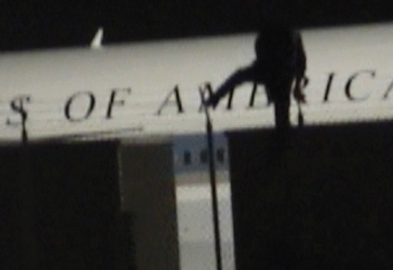 A hooded graffiti writer climbs toward the lettering on the staged Air Force One fuselage.