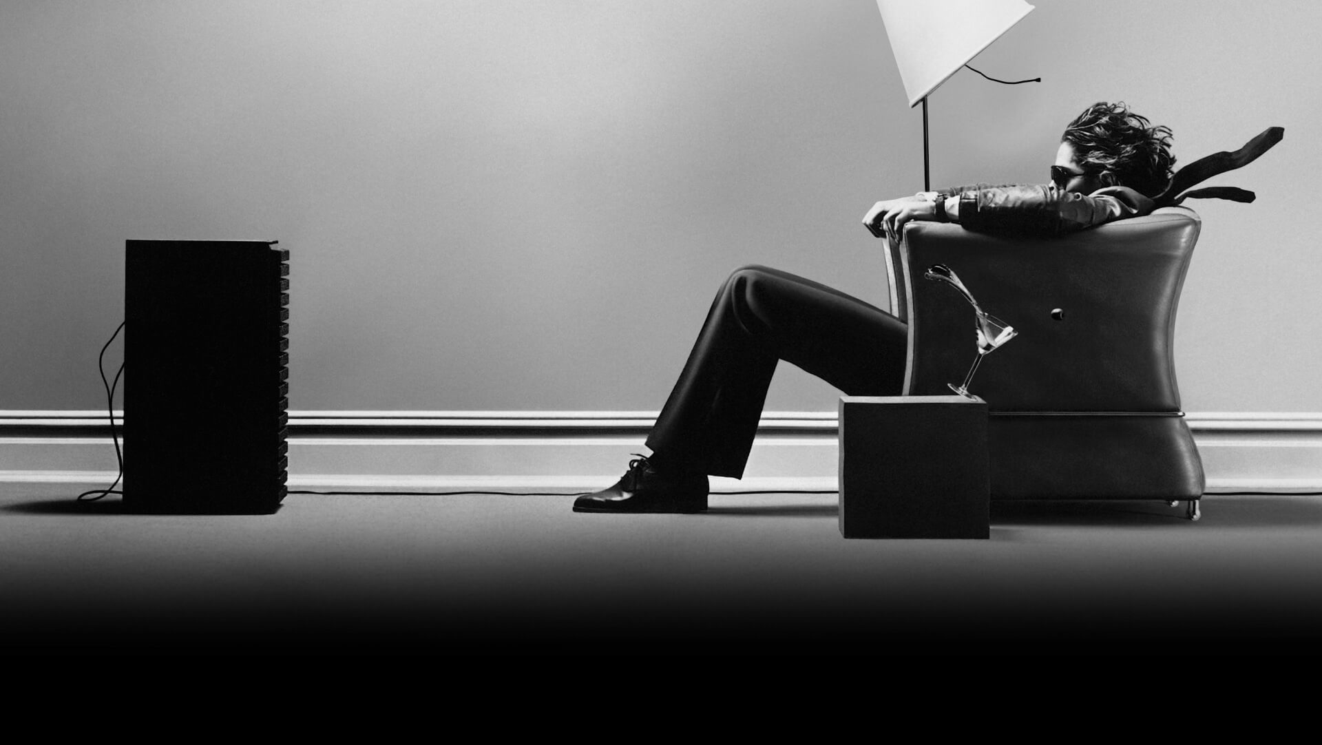Maxell campaign photograph of a seated listener whose hair and clothing stream away from a loudspeaker, with a glass tilting beside him.