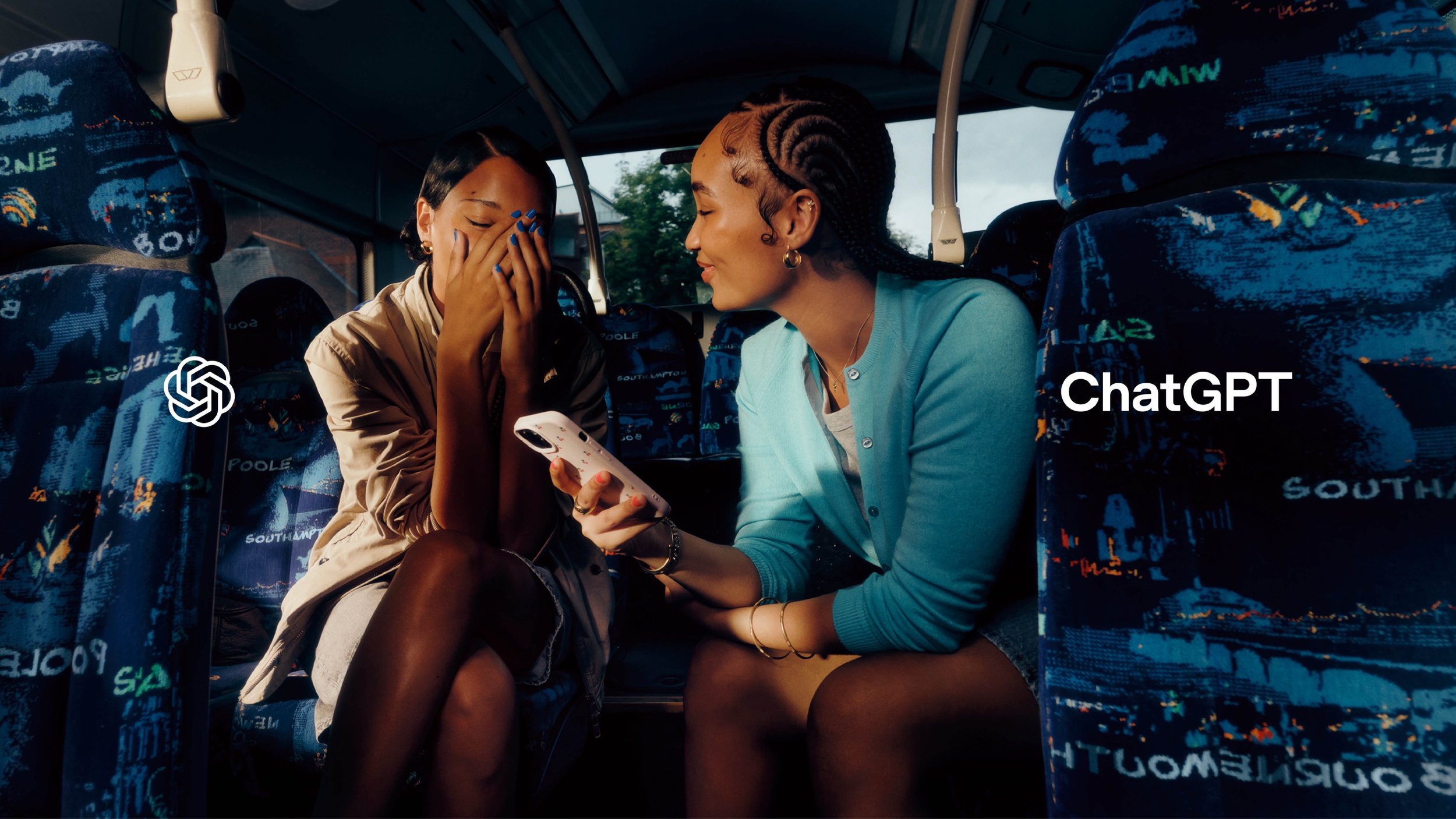 Two friends sit inside a blue-patterned bus; one looks at a phone while the other covers her face in delight. ChatGPT logo and wordmark frame the scene.