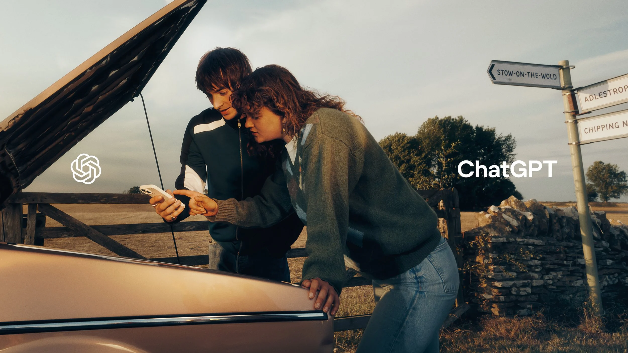 Two people stand beside an open car hood at a rural junction while one looks at a phone. The ChatGPT logo and wordmark sit on either side.