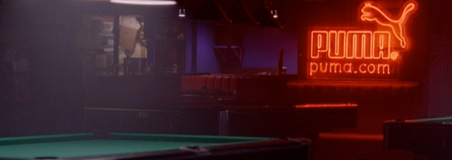 A dark pool hall is lit by a red neon PUMA sign above the table.