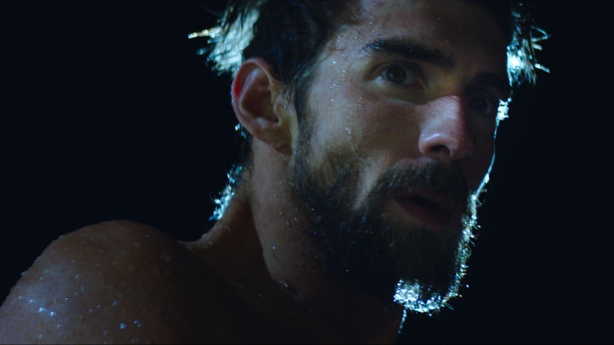 Michael Phelps swims alone beneath lane lines in a dark blue pool.