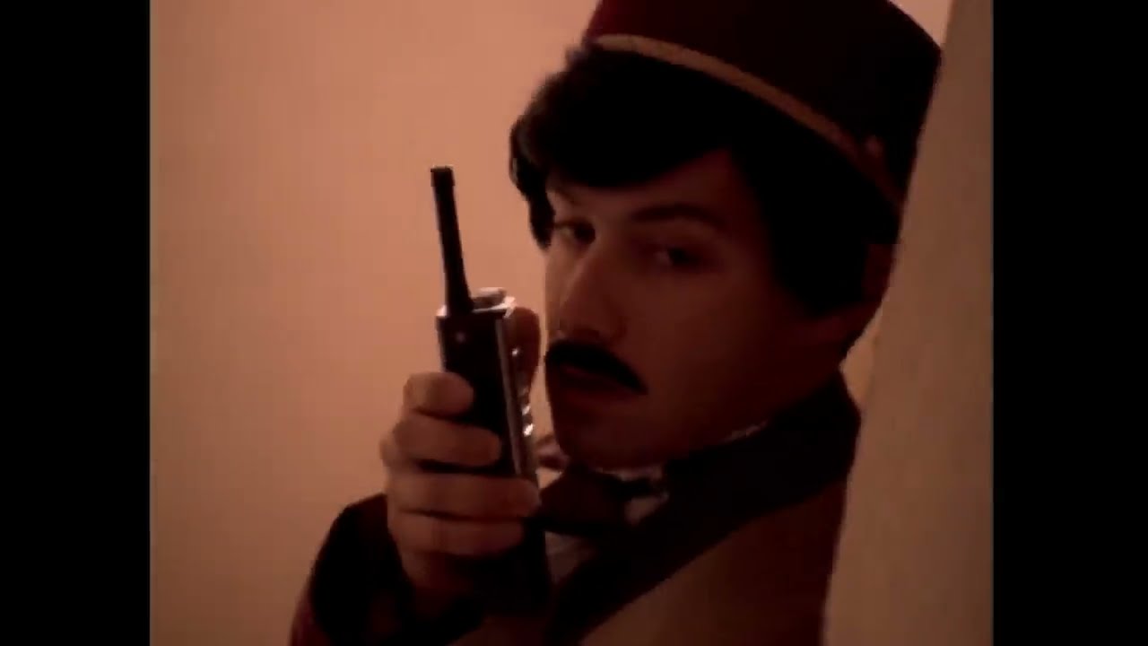 A Beastie Boys performer in a police costume, wig and moustache holding a walkie-talkie in Sabotage.