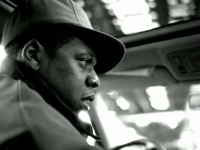 Black-and-white profile of JAY-Z wearing a cap inside a car in 99 Problems.